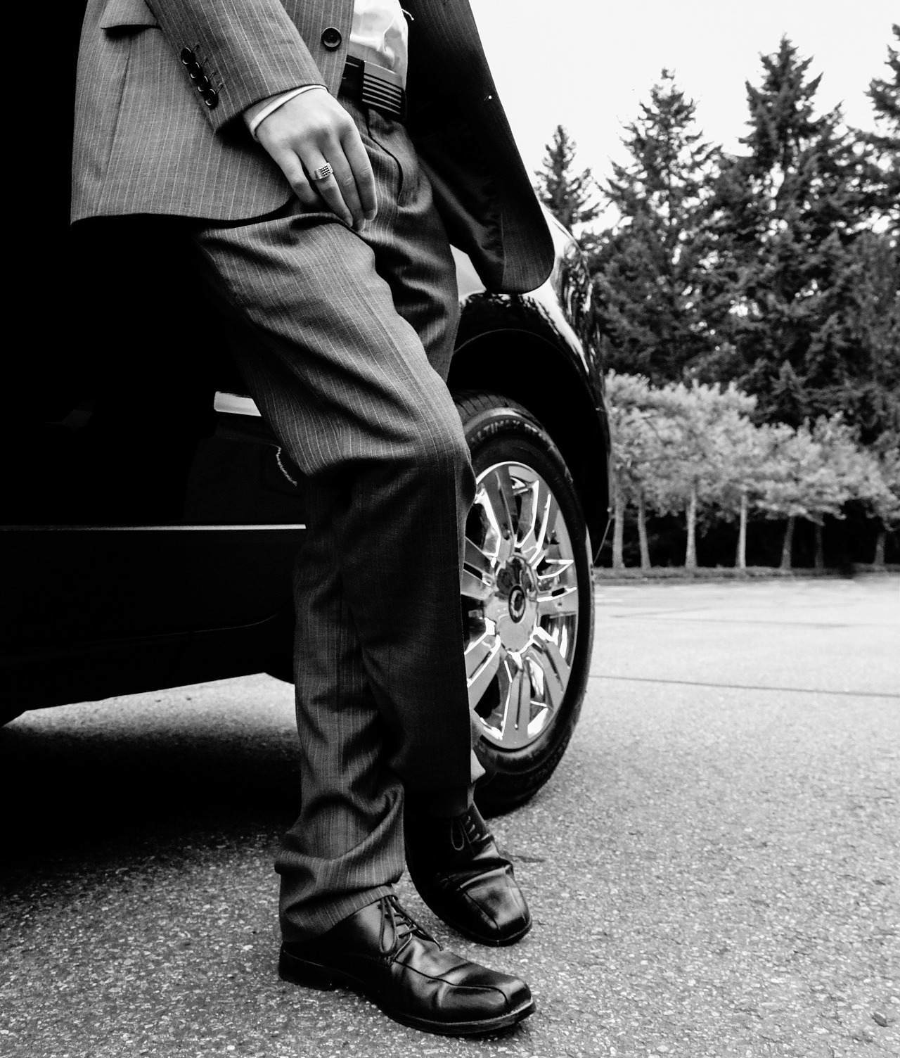 black and white image of man in suit leaning on passenger front door of cadillac